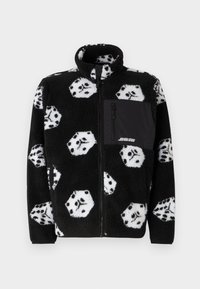 Black fleece zip-up jacket with white dice pattern, high collar, and a front zippered pocket in solid black fabric. Soft texture.