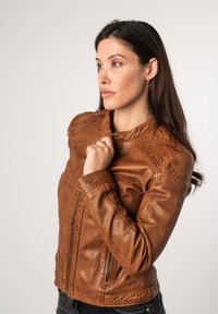 Donkerbruine leren motorjas met een gladde textuur, ritssluiting en schuine naden. Beschikt over een ronde logo op de schouder.