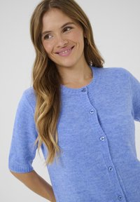 Light blue short-sleeve cashmere cardigan with a round neckline, six blue buttons down the front, and a fine textured knit.