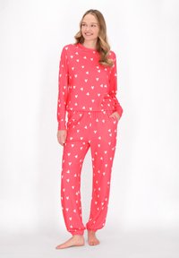 Roze pyjama set bestaande uit een langemouwen shirt en een broek, beide versierd met kleine witte hartjes. Zachte, rekbare stof. Elastische tailleband.