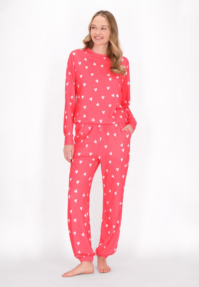 Roze pyjama set bestaande uit een langemouwen shirt en een broek, beide versierd met kleine witte hartjes. Zachte, rekbare stof. Elastische tailleband.