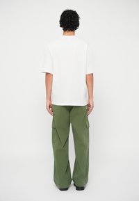 T-shirt branca de algodão com mangas curtas, combinada com calças cargo verdes com bolsos laterais e um ajuste solto. Apenas a vista traseira.