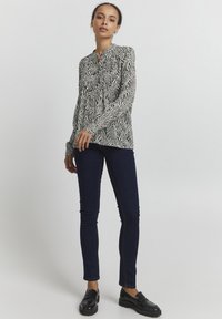 Blusa a righe zebrate in bianco e nero con colletto alto, maniche lunghe e vestibilità comoda, abbinata a jeans skinny scuri e mocassini neri.