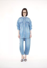 Svetlo modra oversized denim srajca z dvema sprednjima žepoma, v kombinaciji z ohlapnimi svetlo modrimi kavbojkami. Model nosi očala z rumenim odtenkom in modre pete.