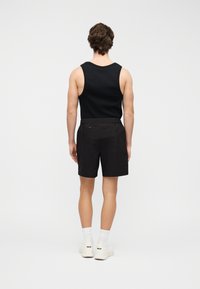 Μαύρο τοπ χωρίς μανίκια και μαύρο σορτς φορεμένα μαζί. Το σορτς διαθέτει ελαστική μέση και δύο πλαϊνές τσέπες. Το σύνολο συμπληρώνουν λευκές κάλτσες και παπούτσια.