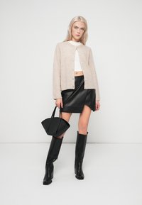 Bež pleteni kardigan s okroglim izrezom, bela kratka majica, črna usnjena minikrila, črne visoke škornje s peto do kolen in črna torba.