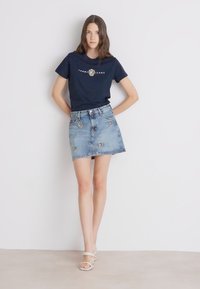 Námornícky bavlnený tričko s logom "TOMMY JEANS", v kombinácii so svetlomodrou džínovou minisukňou s dekoračnými gombíkmi.