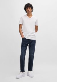 White v-neck t-shirt, dark blue jeans, and white sneakers. Smooth fabric, standard fit, and mid-rise design with basic stitching details.