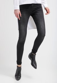 Jeans negros ajustados con una textura suave, con una cintura alta, combinados con elegantes botas negras hasta el tobillo. La parte superior es blanca y larga.