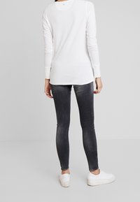 Vit långärmad topp med rund halsringning, som är parat med mörkgrå skinny jeans och vita sneakers. Enkel design, mjukt tyg, smal passform.