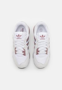 Valkoiset urheilukengät, joissa on mokkanahkaosia, kolmea sinistä ja vaaleanpunaista raitaa, pyöristetty nenä ja valkoiset nauhat. Brändäys kielen päällä.