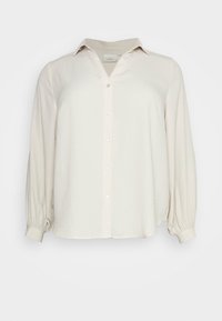 Ljust beige knapp-up skjorta med veckad krage, långa puffärmar och en lätt rundad nederkant. Tillverkad av ett mjukt, strukturerat tyg.