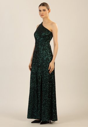Dunkelgrünes Abendkleid mit einem Schulterträger, verziert mit Pailletten, und einem taillierten Schnitt, der einen hohen Schlitz bis zum Oberschenkel hat. Elegante schwarze High Heels ergänzen den Look.