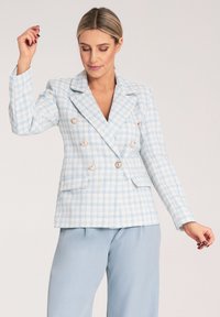 Jasnoniebieska w kratkę marynarka dwurzędowa z złotymi guzikami, wyposażona w dwie przednie kieszenie i wyraźnie ustrukturalizowane klapy. Teksturowany materiał podkreśla szczegóły wizualne.