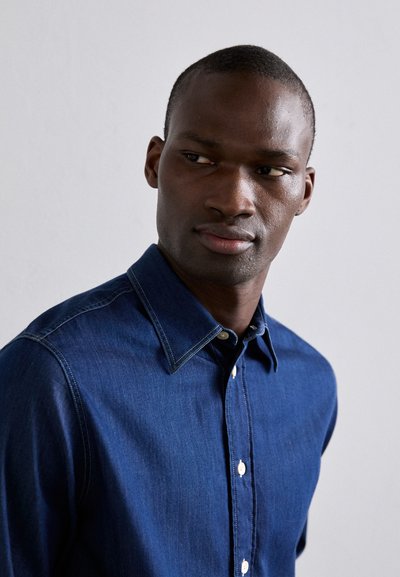 Camicia di denim blu scuro con colletto classico, chiusura frontale con bottoni e cuciture a contrasto lungo le cuciture. Texture liscia.