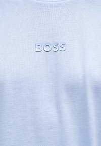 Ανοιχτό μπλε ύφασμα με ανάγλυφα λευκά γράμματα που σχηματίζουν τη λέξη "BOSS" στο κέντρο της επιφάνειας.