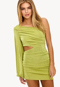 Robe mini asymétrique froncée en vert clair, avec un détail découpé sur le côté. Texture douce avec une finition légèrement brillante.