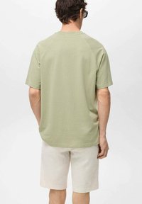 Maslinasto zelena majica kratkih rukava s okruglim izrezom, izrađena od meke tkanine; uparena s svijetlosmešavim šortsevima. Glatka tekstura, opušteni kroj.