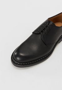 Czarne skórzane buty eleganckie o gładkim wykończeniu, zaokrąglonym nosku i czterema otworami na sznurówki. Posiadają ozdobne przeszycia wzdłuż podeszwy.