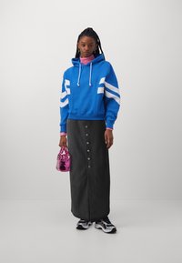 Felpa blu con strisce bianche, gonna grigia con bottoni davanti, dolcevita rosa, borsa rosa e scarpe da ginnastica in bianco e nero.