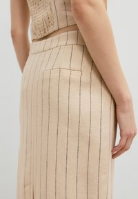 Beige Rock mit vertikalen schwarzen Streifen, aus strukturiertem Stoff gefertigt. Verfügt über eine Gesäßtasche und einen taillierten Bund.
