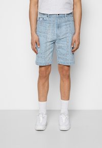 Lichtblauwe denim shorts met een bandana-patroon, standaard pasvorm en twee voorzakken, gecombineerd met witte sokken en sneakers.