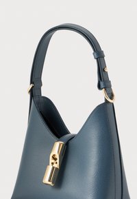 Sac à main en cuir texturé bleu avec un fermoir en ton doré, présentant une forme unique et une bandoulière robuste. Les accents incluent des accessoires en métal.