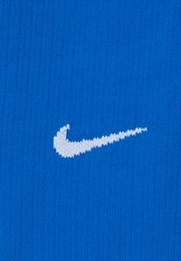 Blauw gebreid stof met een opvallend wit Nike swoosh-logo, waarbij de contrasten tussen de kleuren en de gladde textuur worden benadrukt.