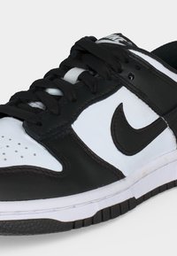 Zwart-witte Nike-sneaker met zwarte veters en een zichtbare zwarte Nike-swoosh aan de zijkant.