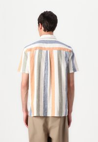 Camisa de manga curta em linho riscado. Apresenta cores alternadas de laranja, azul, verde e branco. Detalhe notável na yoke das costas.