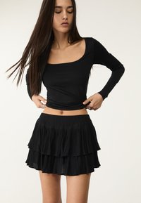 Zwarte top met lange mouwen en vierkante halslijn, gecombineerd met een zwart gelaagde mini rok met een ruchesontwerp en elastische tailleband.