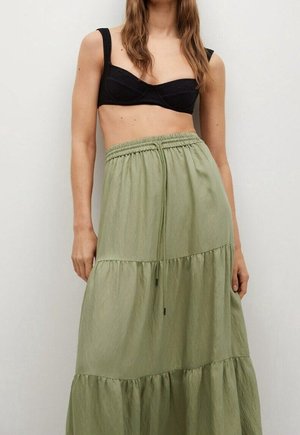 Vrouw draagt een zwart cropped top met brede bandjes en een hoge taille, olijfgroene rok met laagjes en een tailleband met trekkoord.