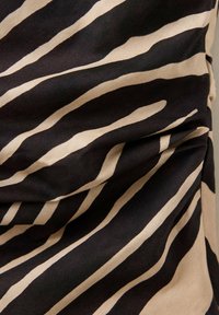Tissu noir et beige avec des rayures ondulées irrégulières, légèrement torsadé pour créer des plis et de la texture.