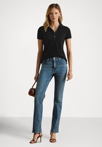 Svart polo-t-skjorte med korte ermer og knappet stolpe, kombinert med lyseblå jeans med rette ben og brune sandaler med hæl.