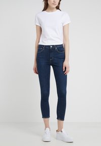 Camiseta de algodón blanca con mangas enrolladas, combinada con vaqueros ajustados de mezclilla azul oscuro de cintura alta y zapatillas de plataforma blancas.