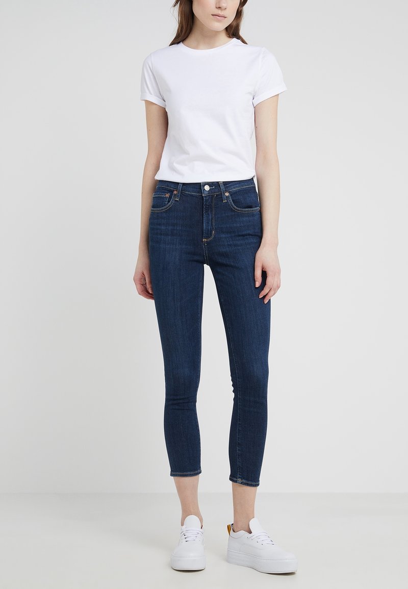 Camiseta de algodón blanca con mangas enrolladas, combinada con vaqueros ajustados de mezclilla azul oscuro de cintura alta y zapatillas de plataforma blancas.