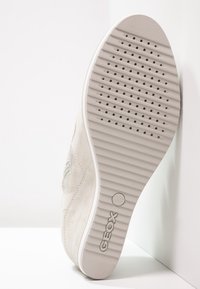 Jasnoszary sneaker z fakturowaną cholewką zamszową, gumową podeszwą z otworami wentylacyjnymi oraz wzorem bieżnika. Logo marki widoczne na pięcie.