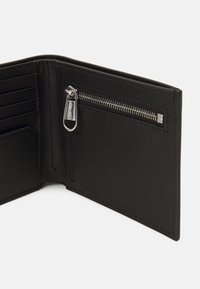 Portafoglio in pelle nera con più slot per carte, una tasca con zip e cuciture ordinate. Presenta accessori metallici argento per la zip.