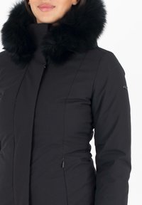 Giacca a vento nera con un ampio colletto in pelo nero, dotata di zip frontale e tasche laterali. Tessuto morbido con una silhouette aderente.