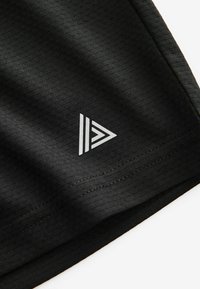 Shorts de sport noirs en tissu texturé. Un logo triangulaire blanc est positionné près de l'ourlet, avec des détails de couture visibles.