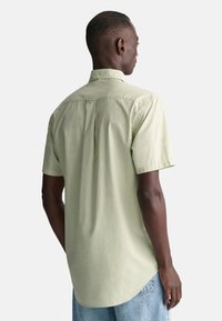Camisa de manga corta en algodón verde claro con cuello abotonado, pliegue trasero y dobladillo curvado, combinada con jeans azul claro.