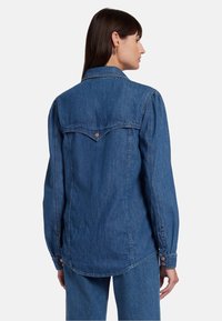 Denim shirt in medium blauw met lange mouwen, puntige kraag en met knopen sluitende manchetten. Beschikt over schouderpas details en contrasterend stiksel.
