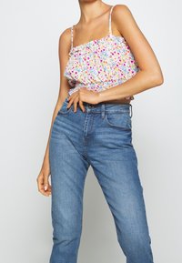 Blommig crop top med justerbara band, med en rynkad midja och flerfärgade blomster mönster. Matchas med midblå denimjeans.