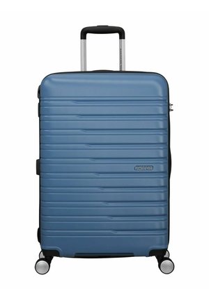 Maleta rígida en azul claro mate con marcas verticales, acentos en negro, asa retráctil y cuatro ruedas para una fácil movilidad.