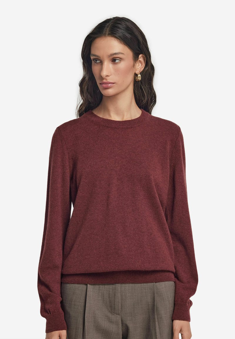 Burgunderfarbener Pullover mit rundem Ausschnitt, gerippten Bündchen und Saum; aus weichem, strukturiertem Material; kombiniert mit hellgrauen, plissierten Hosen.