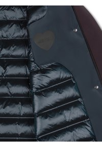 Giacca puffer blu navy con tessuto esterno imbottito, pannelli lisci e un'etichetta a forma di cuore con testo in rilievo. Dettaglio in bottone a pressione argentato.