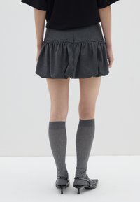 Falda gris acampanada con detalle de volantes fruncidos, combinada con medias gris hasta la rodilla y tacones negros de punta con acentos de tachuelas.