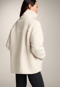 Giacca in pile color crema con colletto alto, vestibilità oversize e superficie textured. Presenta un orlo diritto e spalle leggermente scese.