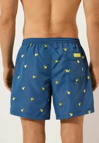 Blauwe zwemshorts met een verstelbare tailleband, versierd met gele schelpenpatronen. Inclusief een achterzak met een geel label.