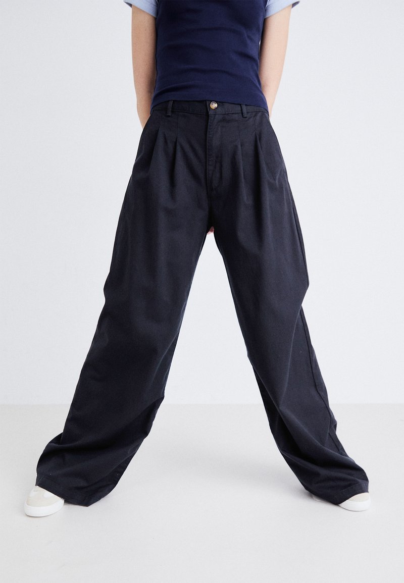 Pantalons larges noirs en tissu léger, dotés de plis avant, d'une fermeture à bouton et de poches latérales.